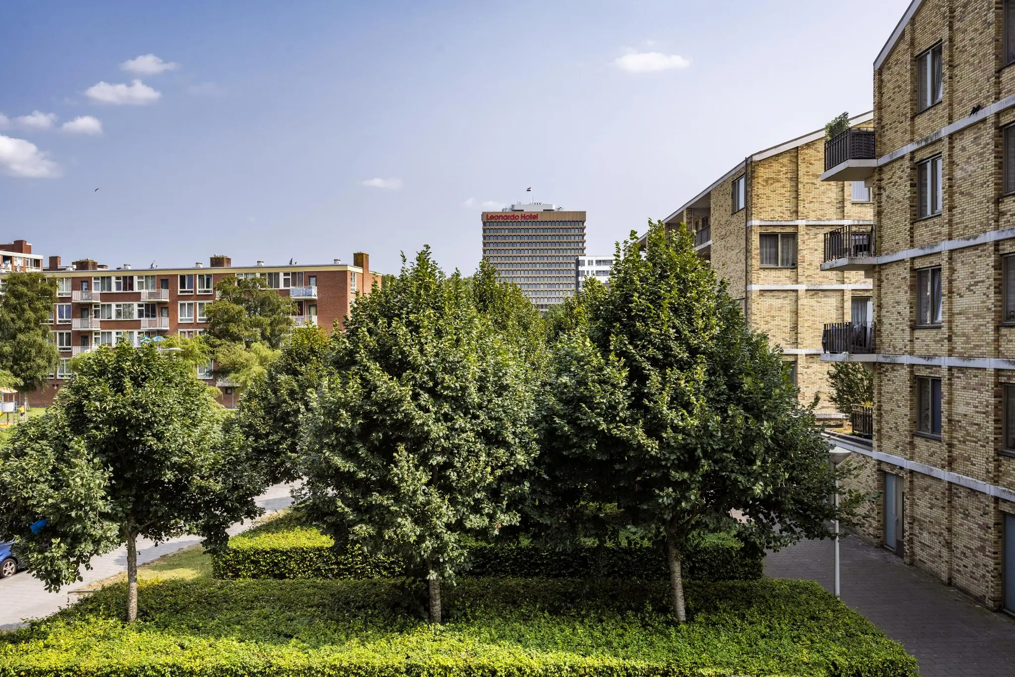 Uitzicht op de Jan Tooropstraat in Amsterdam met groene bomen, omliggende flats en het Leonardo Hotel op de achtergrond.